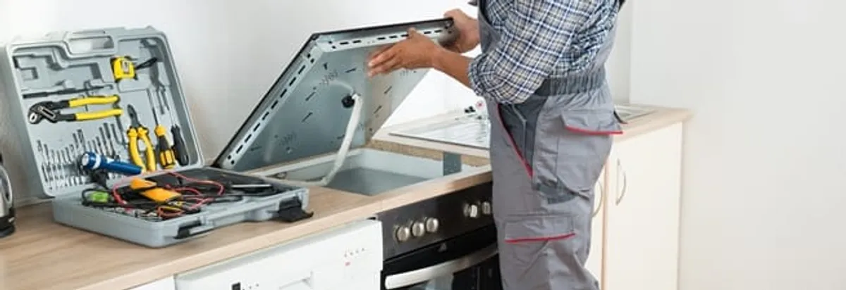 Cooktop repair technician lifting a built-in stovetop for service in Aurora, CO
