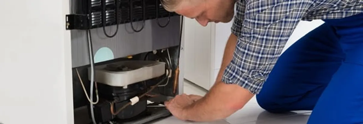 Refrigerator repair technician servicing the compressor and condenser area in Aurora, CO