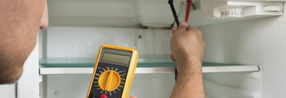 Refrigerator repair technician testing electrical components with a multimeter in Aurora, CO